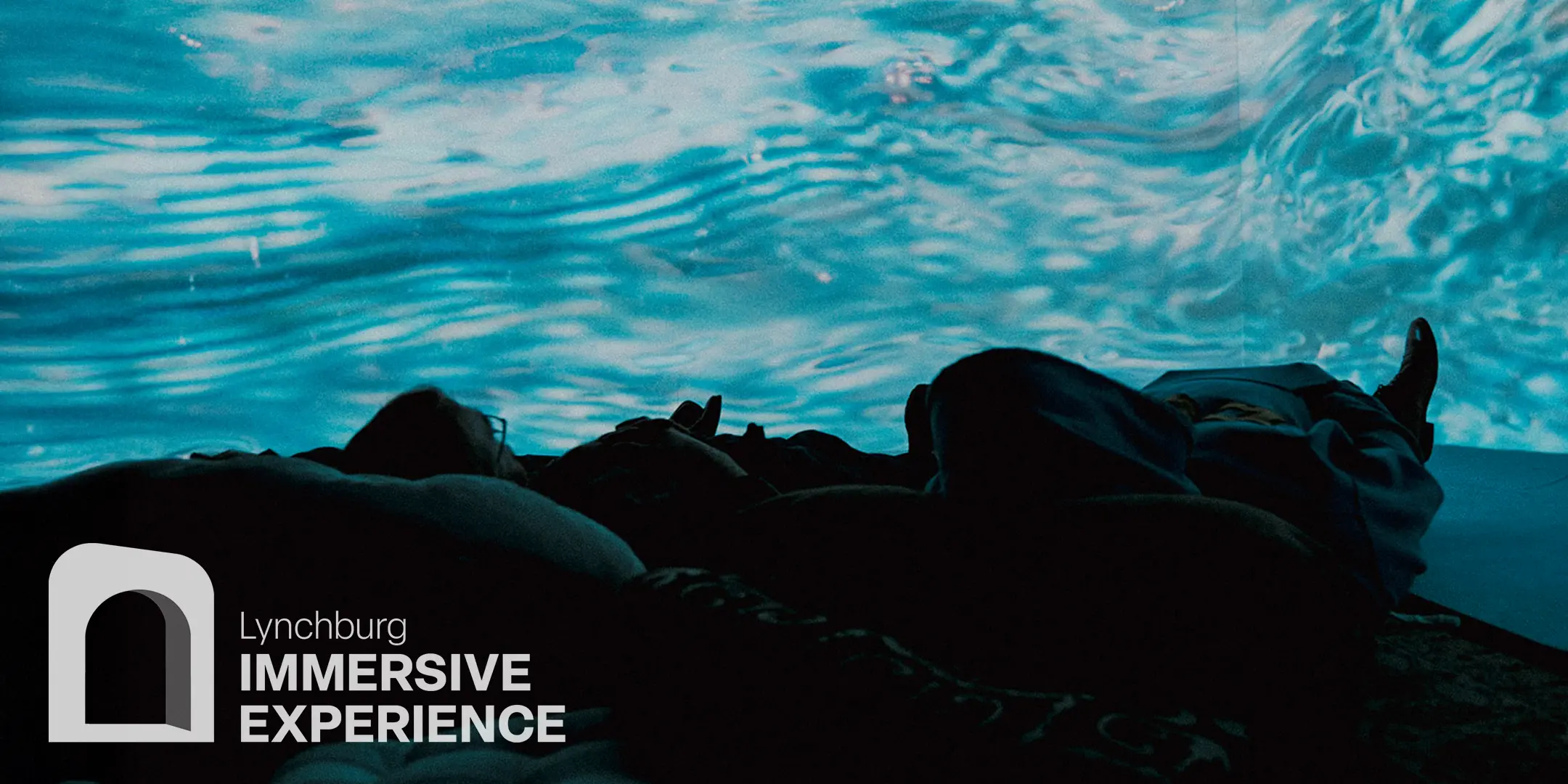 People lying back inside the immersive room, watching rippling water projected across the walls.